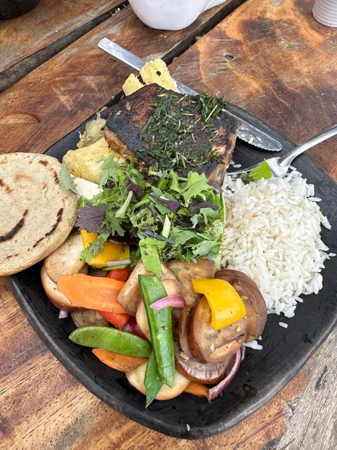 A plate of grilled fish, vegetables, rice and tortillas on a wooden table