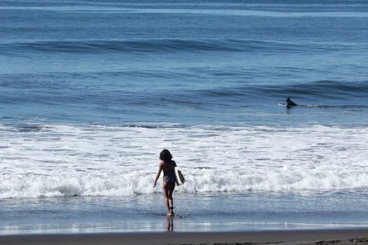 A surfer walking into the sea with her board at Mizata